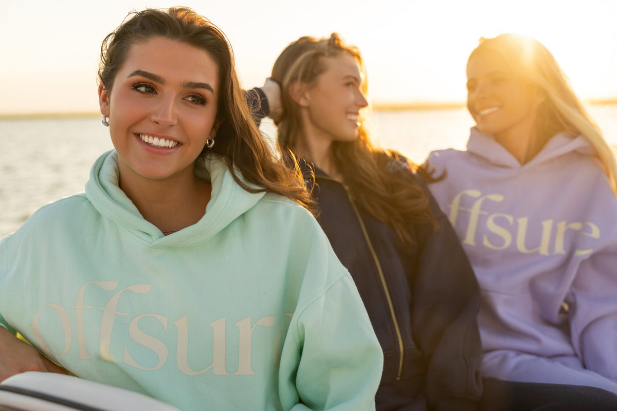 Friends in Sea Glass, Navy Coast, and Light Purple Offsure fleece on a boat at golden hour