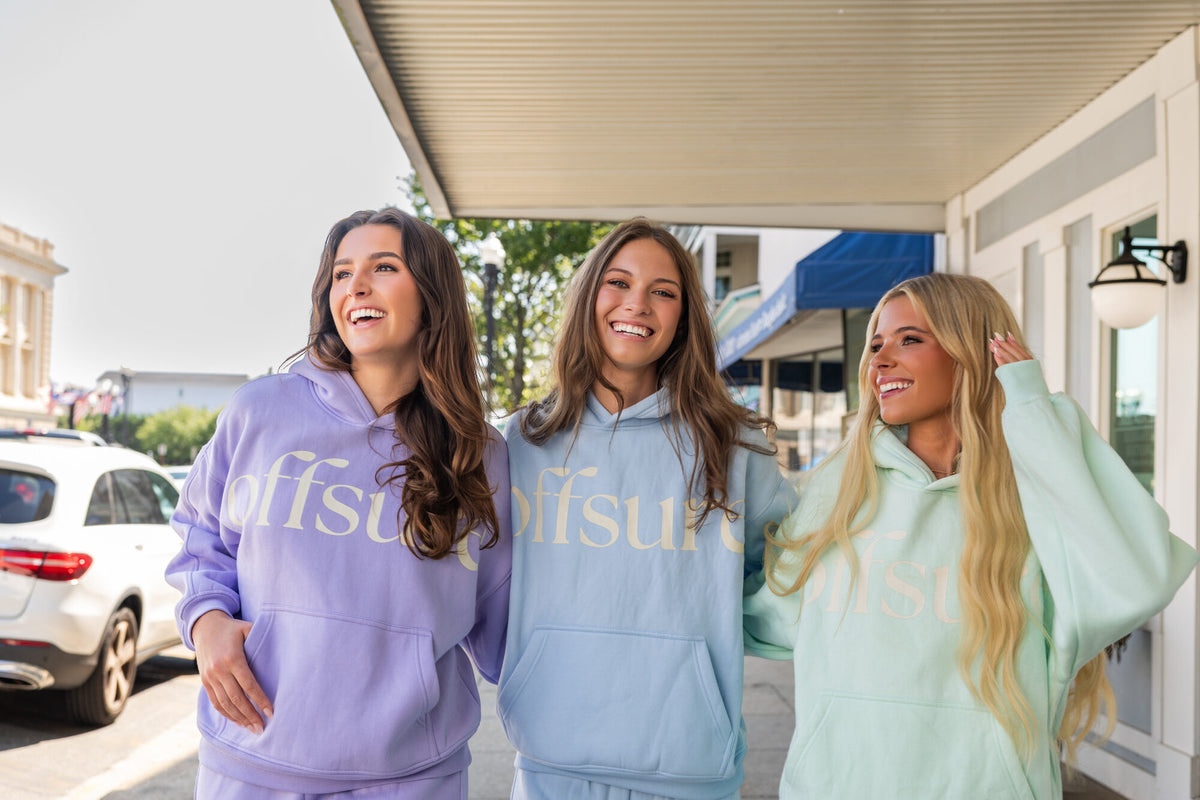 Three friends laughing under a downtown awning in Light Purple, Baby Blue, and Sea Glass Offsure fleece