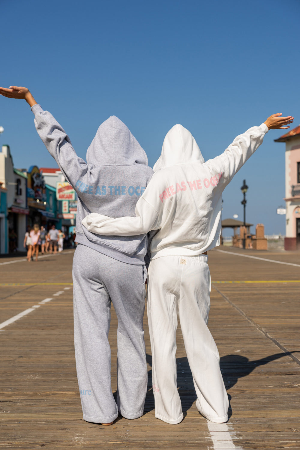 FREE AS THE OCEAN rear artwork on Light Grey Heather and White Beach hoodies on the boardwalk