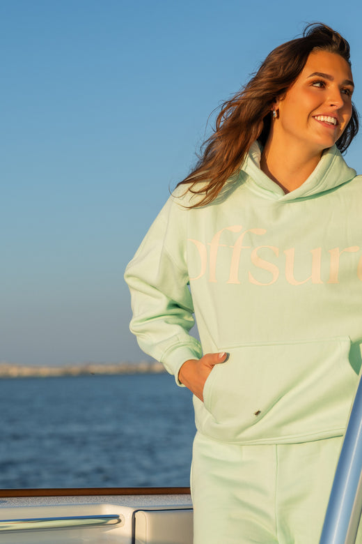 Offsure hoodie and pant in Sea Glass, standing at the bow rail at golden hour